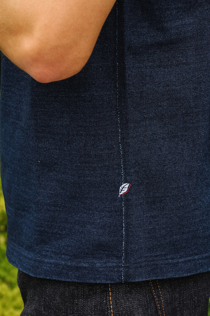 Close-up of a person wearing a dark navy blue ribbed knit top, showing the side seam and a small embroidered logo near the hem.