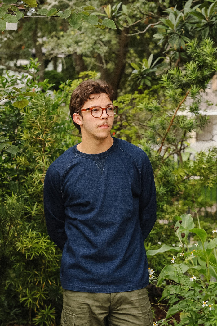 man wearing dark blue long sleeved shirt standing with a green foliage background