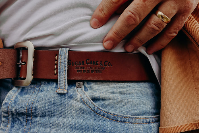 Close-up of brown Sugar Cane & Co. leather belt worn with light blue denim jeans and a white shirt