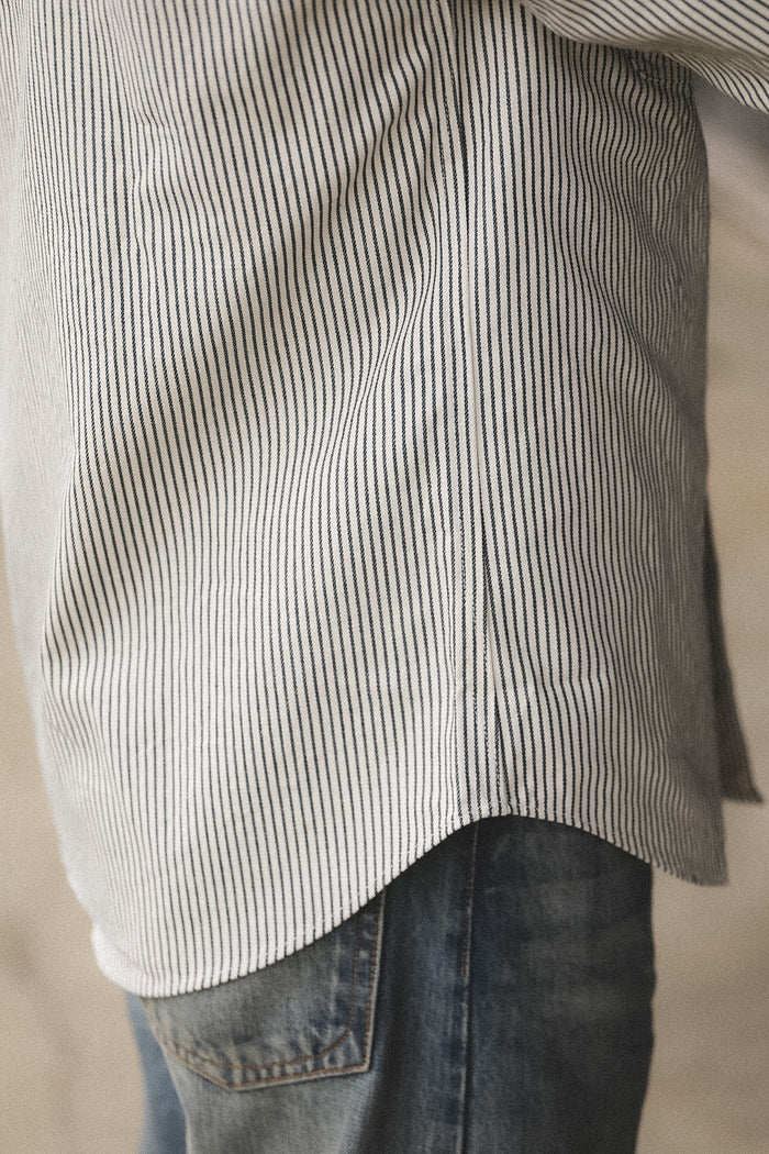 Close-up of a person wearing a striped shirt and jeans against a neutral background