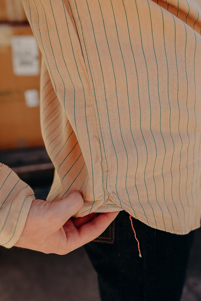 Close-up of hand adjusting beige pinstriped work shirt hem with red thread detail from Iron Shop Provisions
