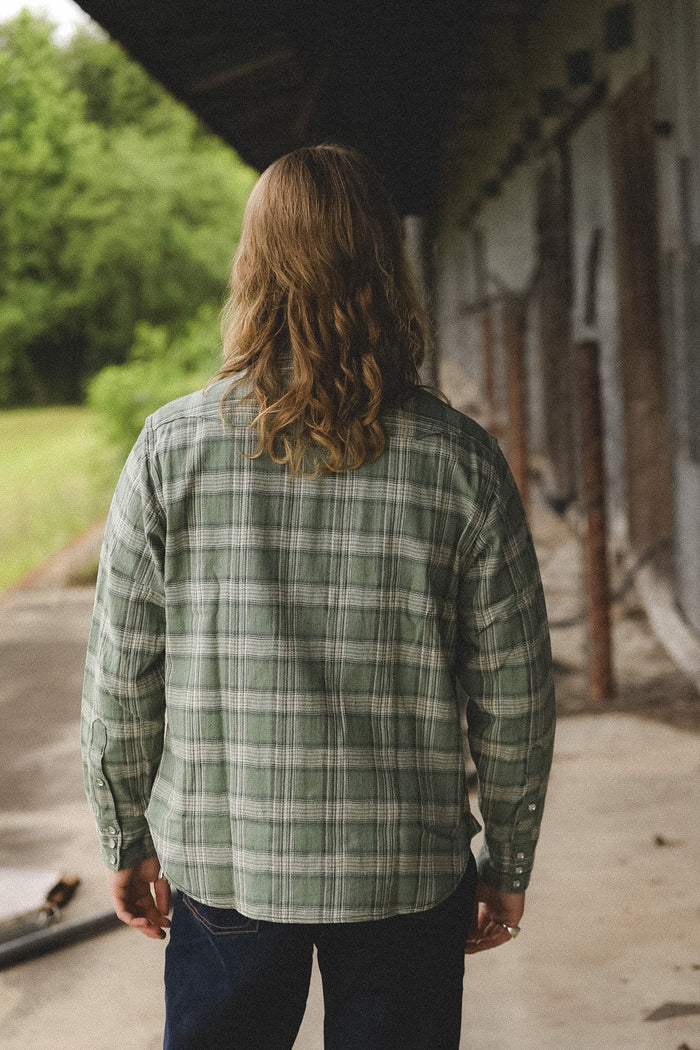 Person wearing a green plaid shirt walking away from the camera in an outdoor setting.