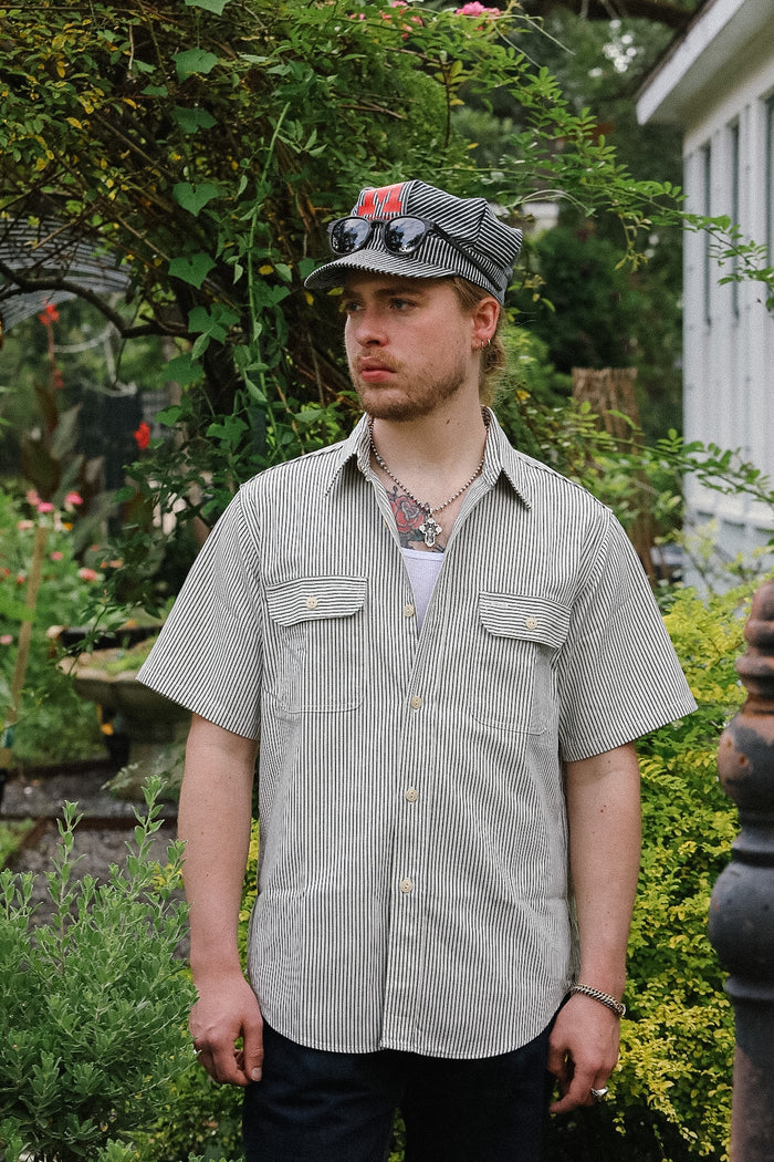 Man wearing a striped shirt and cap standing in a garden