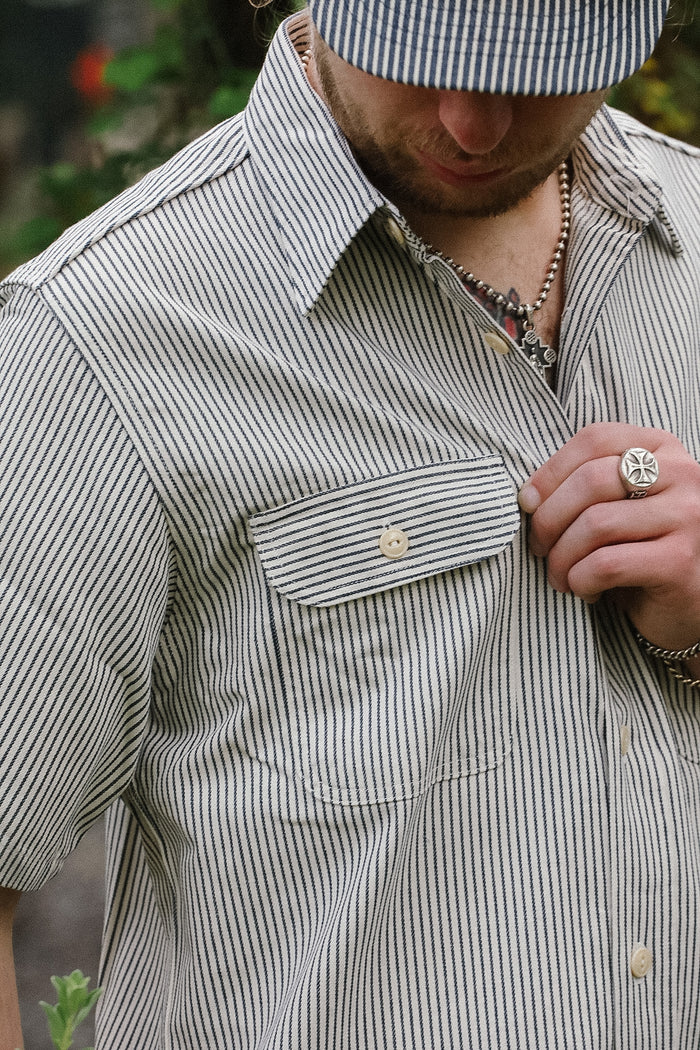Man wearing a striped shirt and cap, with a focus on the shirt's pocket and collar.