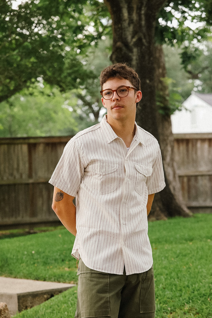 Man wearing glasses and a light shirt standing outdoors with trees and grass in the background