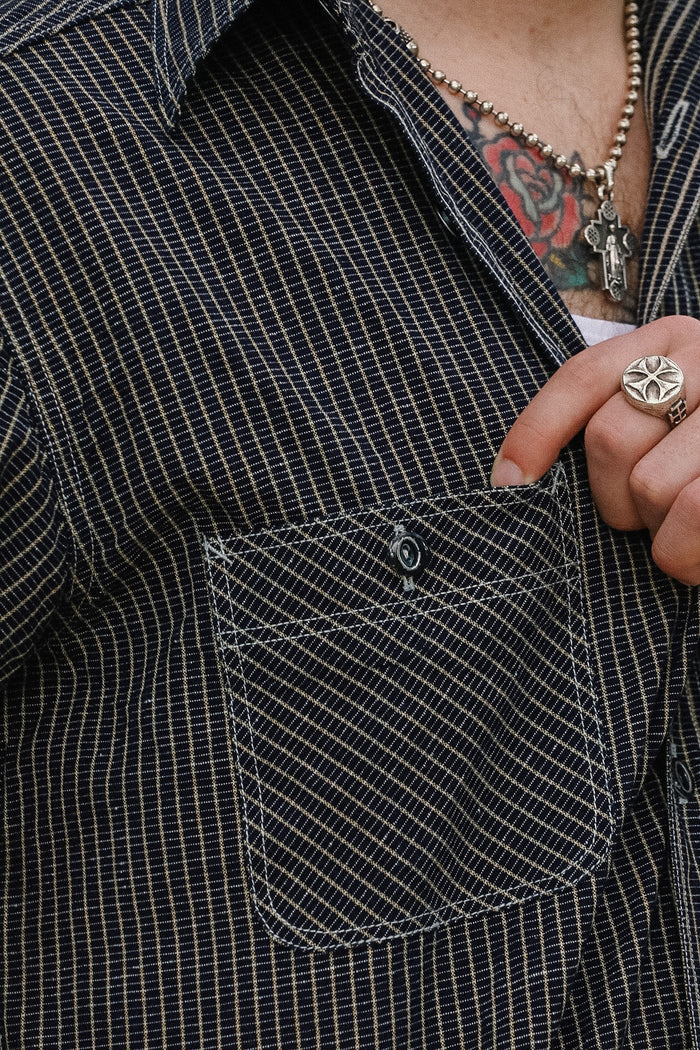 Person wearing a black checkered shirt with a pocket, showing a tattooed arm and ring.