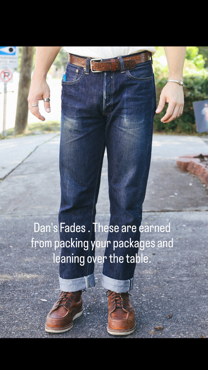 Close-up of dark blue faded jeans with brown leather belt and boots on pavement, urban outdoor setting