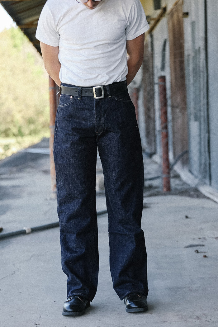 Person wearing a white t-shirt and dark blue jeans standing on a concrete surface.