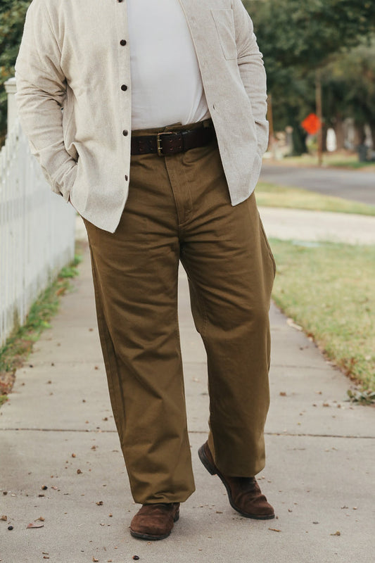 Person wearing a beige jacket, white shirt, and brown pants on a sidewalk.