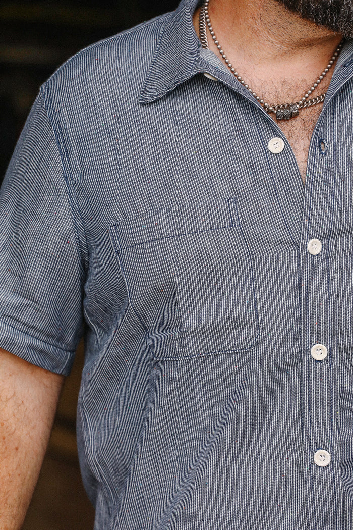 Close-up of man wearing blue and white striped short sleeve button-up shirt with chest pocket and silver necklace