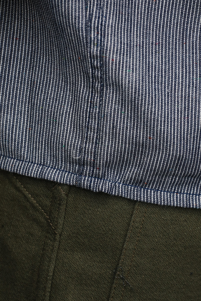 Close-up of striped blue and white short sleeve shirt hem with colorful specks above olive green pants stitching