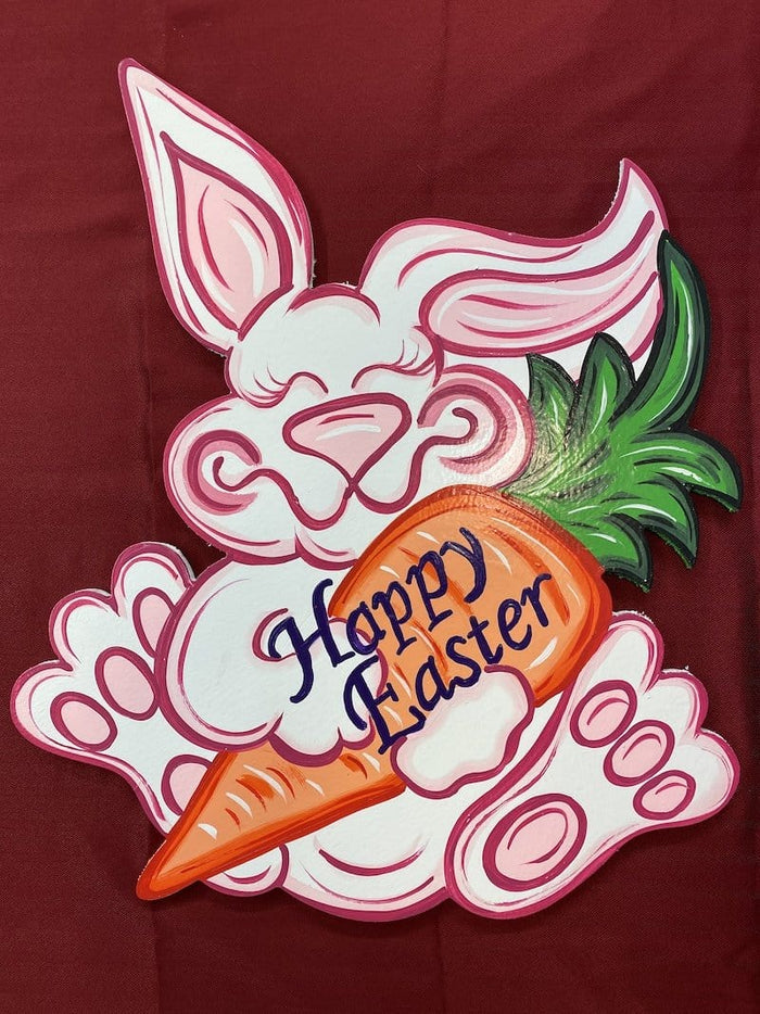sitting pink easter bunny holding a large carrot that says happy easter