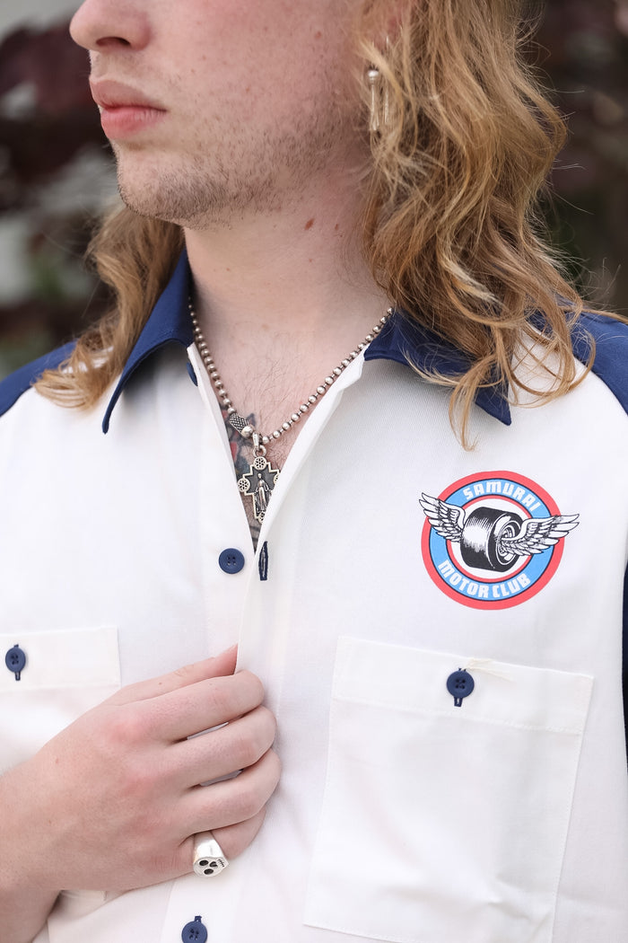 Person wearing a white shirt with a logo and buttons, with a blurred background