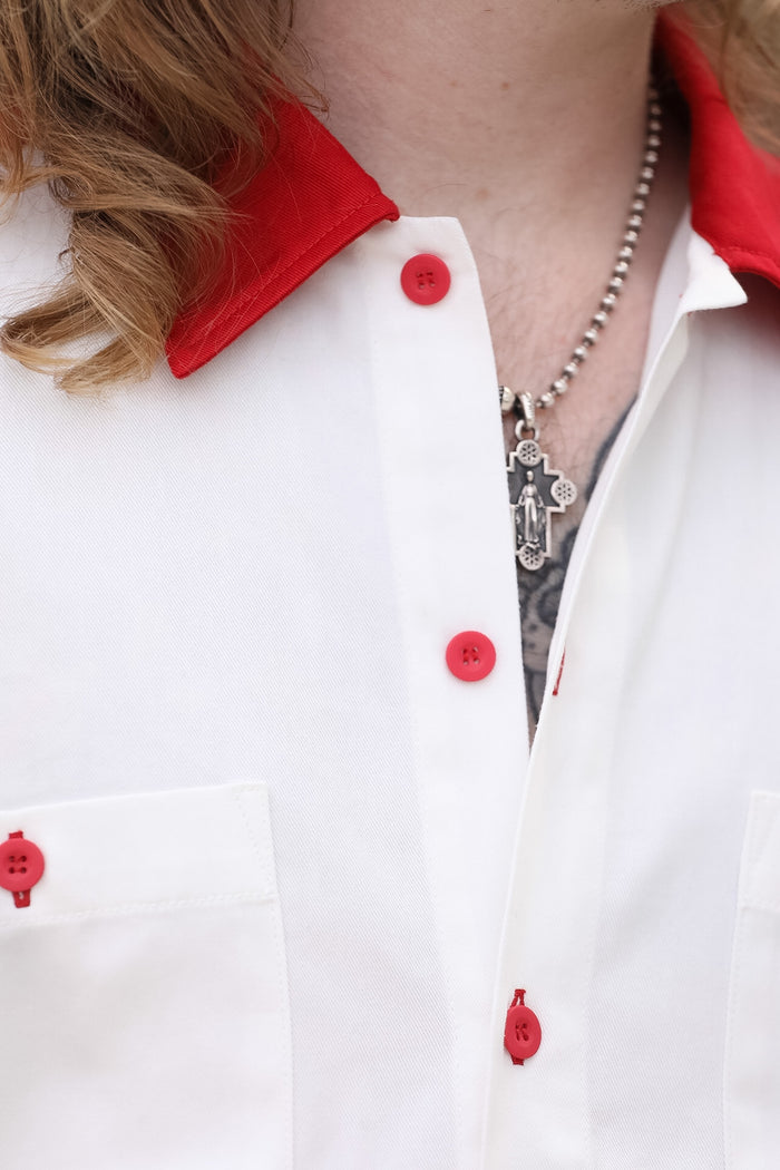 Close-up of a white shirt with red buttons and a necklace.