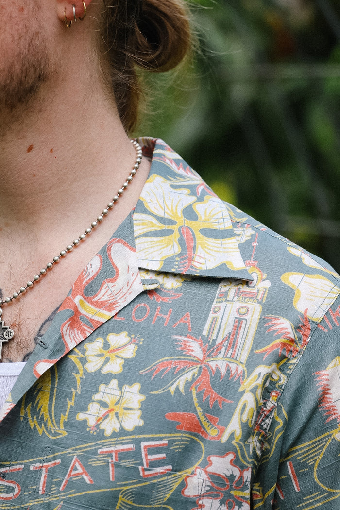 Close-up of a person wearing a colorful aloha shirt with floral and text patterns.