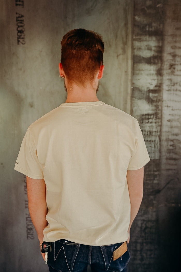 Back view of man wearing beige t-shirt and dark jeans standing against textured industrial wall