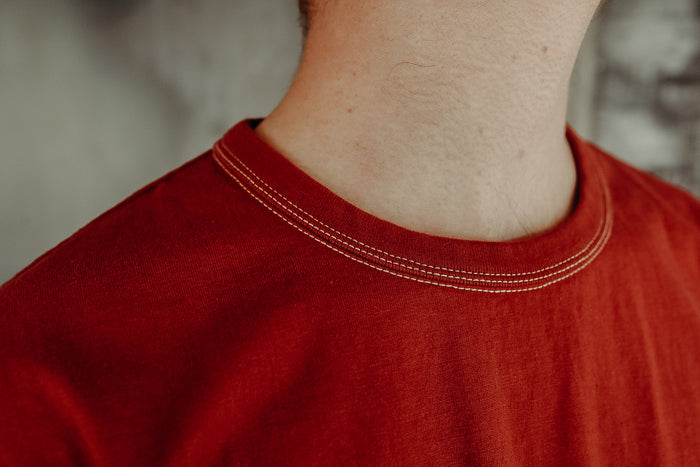 Close-up of a person wearing a red crew neck T-shirt with visible double-stitching detail from Iron Shop Provisions