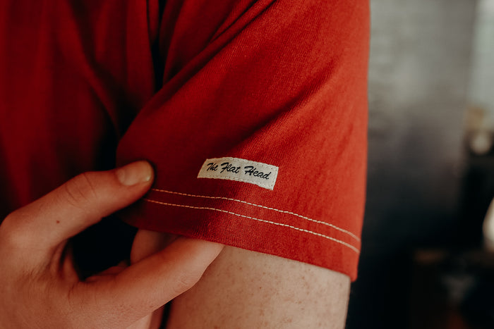 Close-up of red short sleeve shirt with 'The Flat Head' label and hand holding the fabric