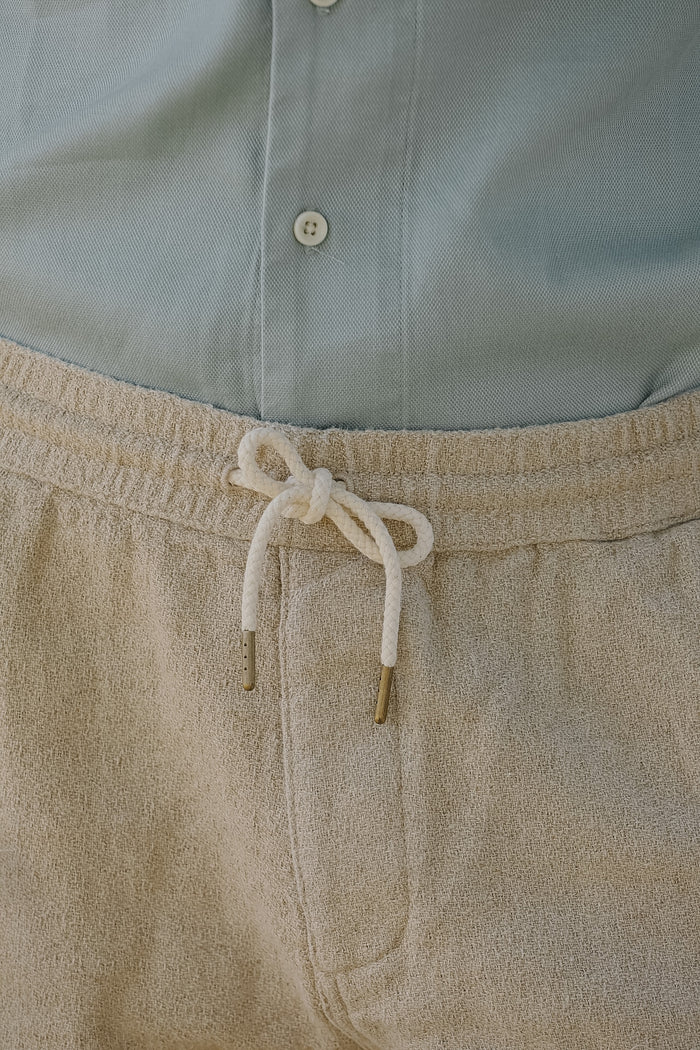 Close-up of beige pants with a drawstring and light blue shirt.