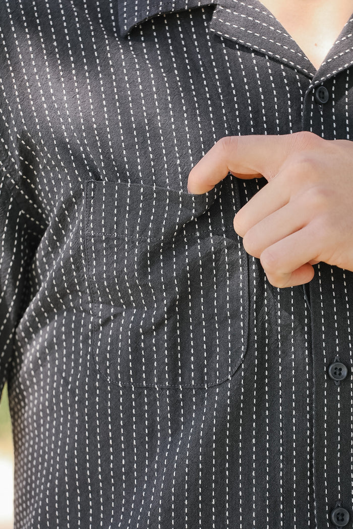 Close-up of a person wearing a black and white striped shirt with a buttoned pocket.