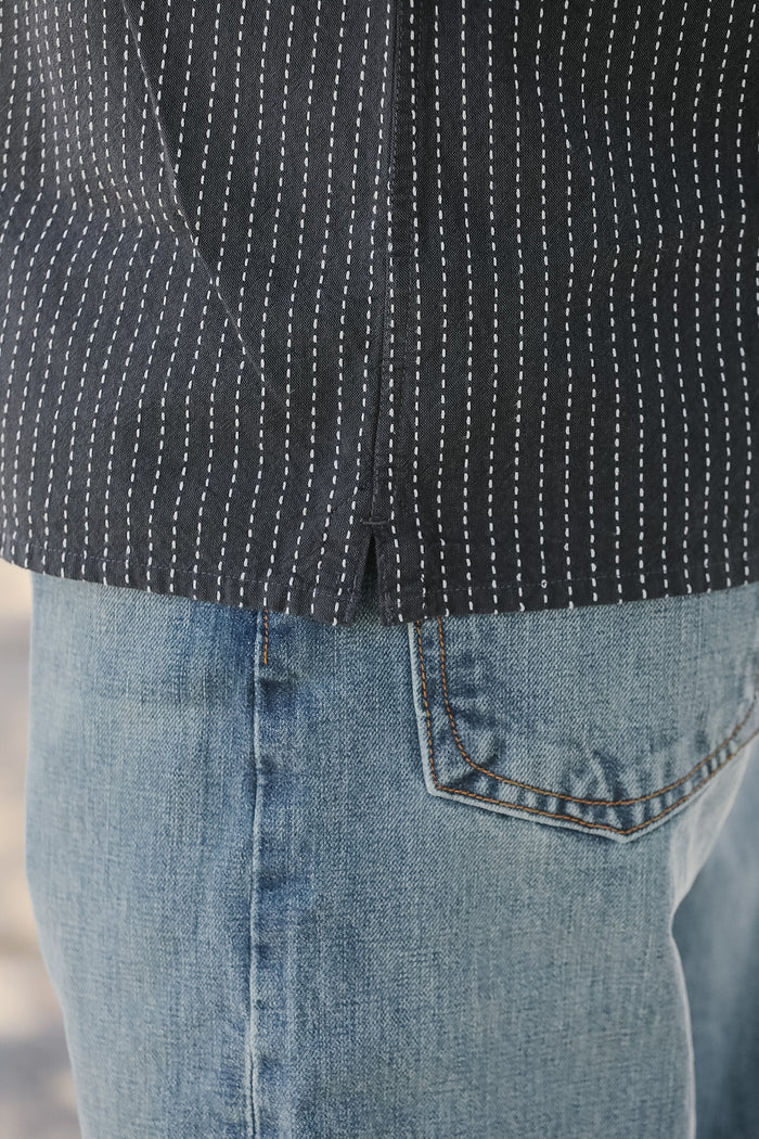 Close-up of a person wearing a black patterned shirt and blue jeans.