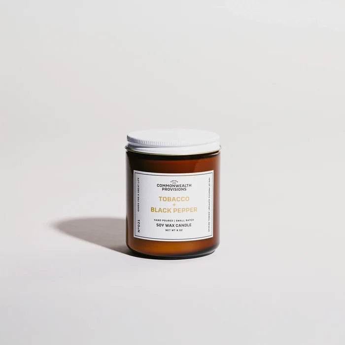 Amber glass jar of Commonwealth Provisions Tobacco and Black Pepper soy wax candle with white lid on light background