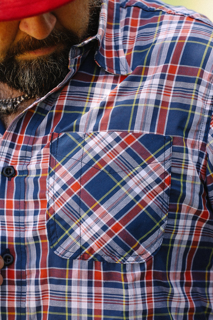Close-up of man wearing navy, red, and white plaid short sleeve shirt with front chest pocket