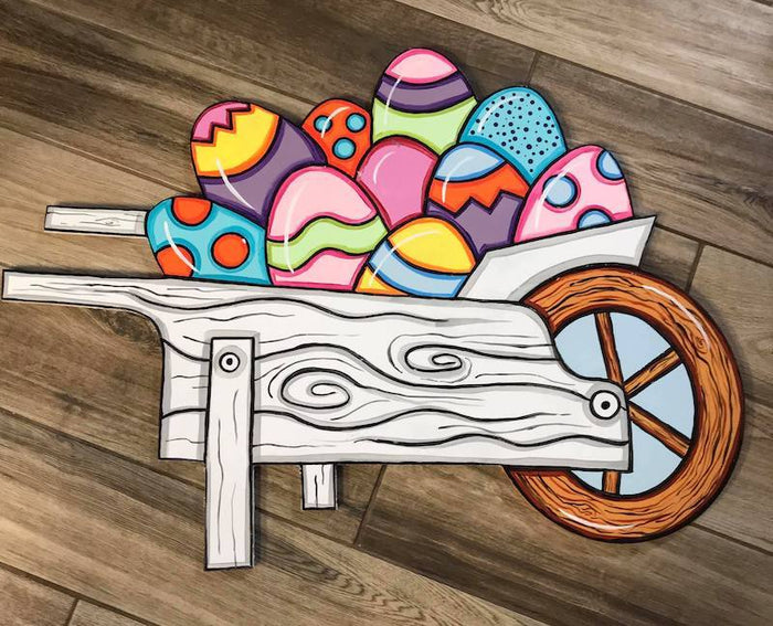 decorated easter eggs in a white wooden wheelbarrow shows on a wooden background
