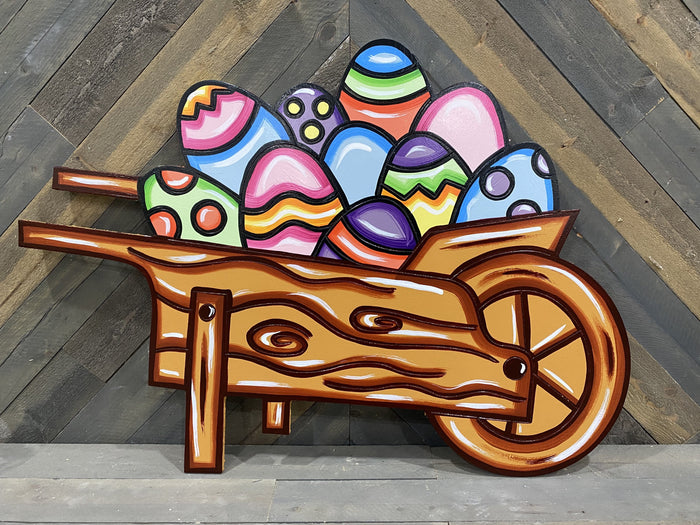 Painted easter eggs in a wooden wheelbarrow shows infront of a wooden wall