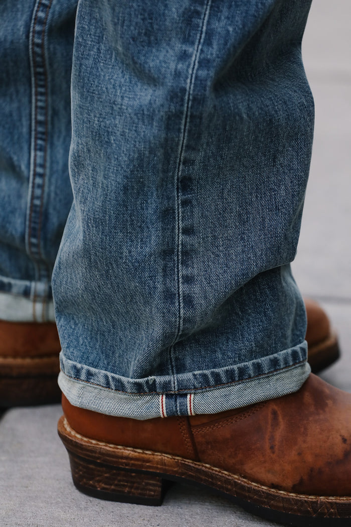 Close-up of blue jeans with rolled-up hem and brown boots on a light gray background