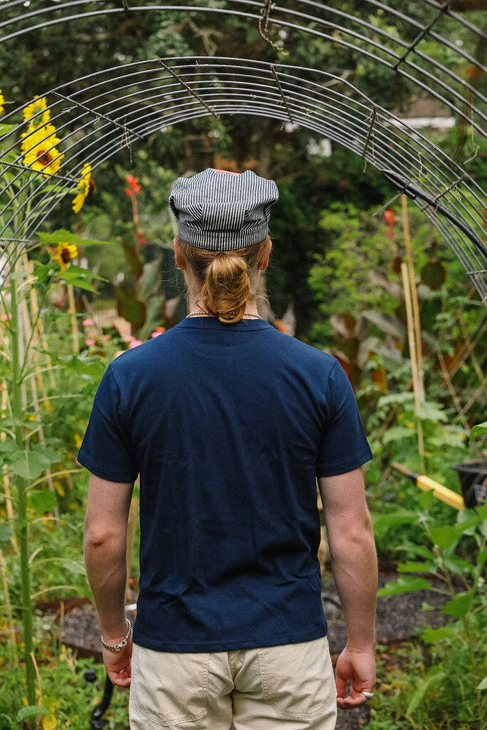 Person wearing a blue shirt and cap walking through a garden with plants and sunflowers.